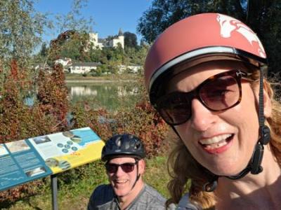 Smiling cyclists in front of an information-board and a castle at the riverbank in the background
